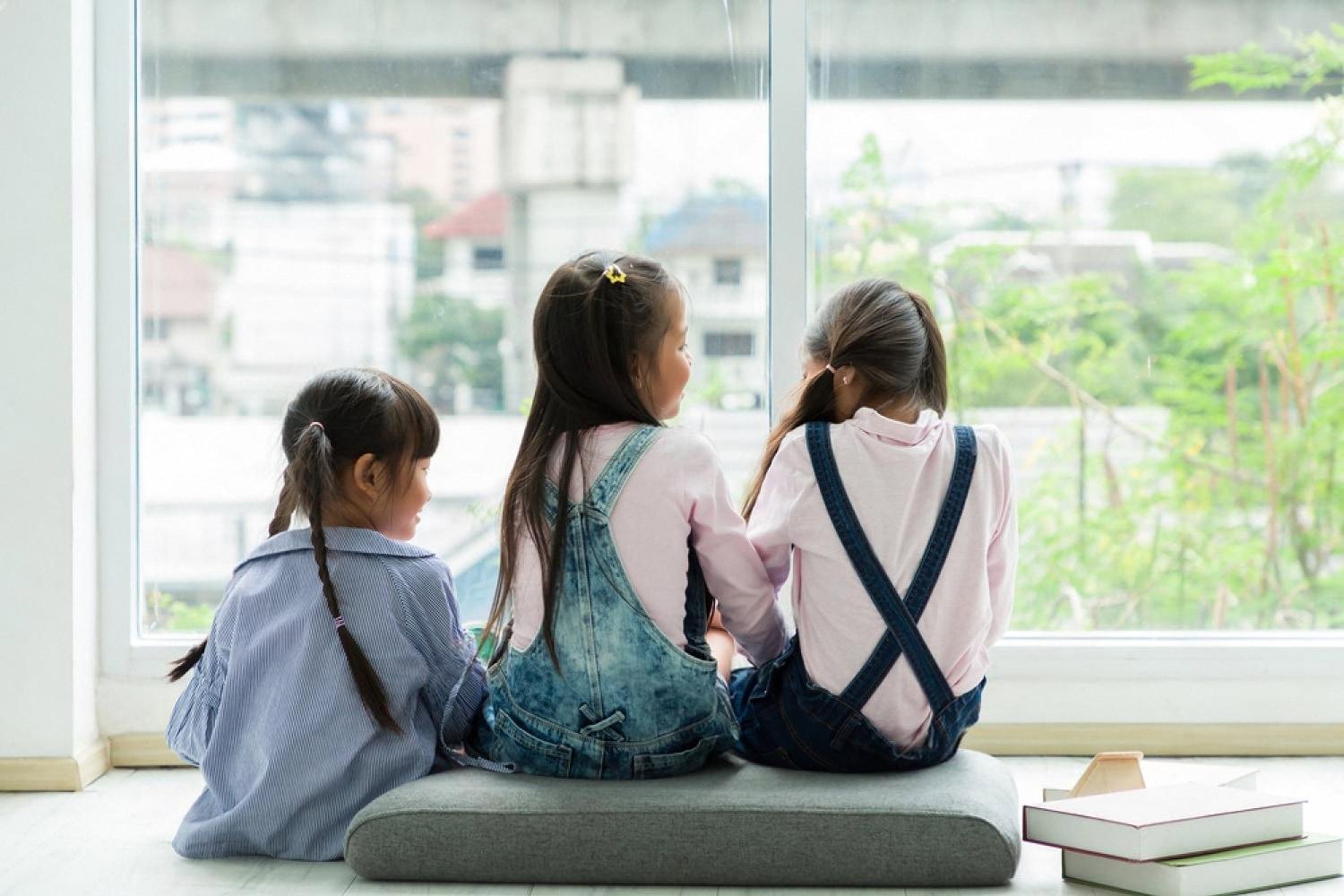Three young girls sitting by a window at school looking out at the city